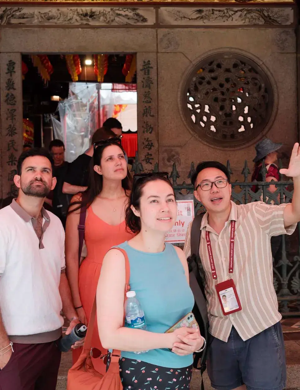 Yong, wearing a Singapore Tourist Guide lanyard, gestures upward as a small group of tour guests looks up at the entrance of a Chinese temple